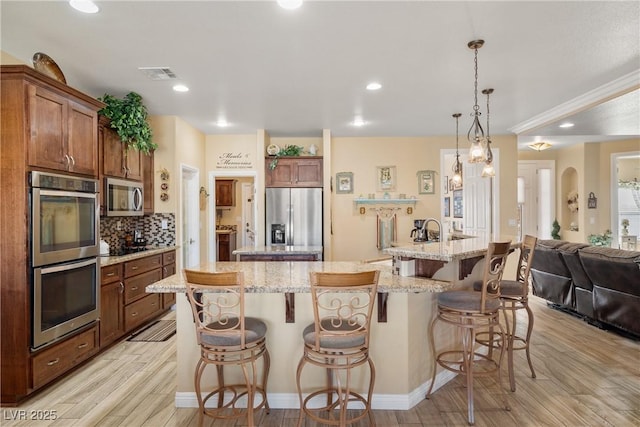 kitchen with pendant lighting, a large island with sink, a kitchen breakfast bar, light hardwood / wood-style flooring, and stainless steel appliances