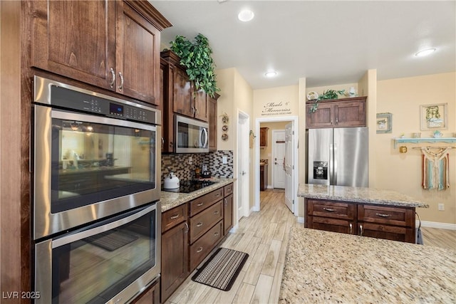 kitchen with tasteful backsplash, light stone counters, light wood-type flooring, and appliances with stainless steel finishes