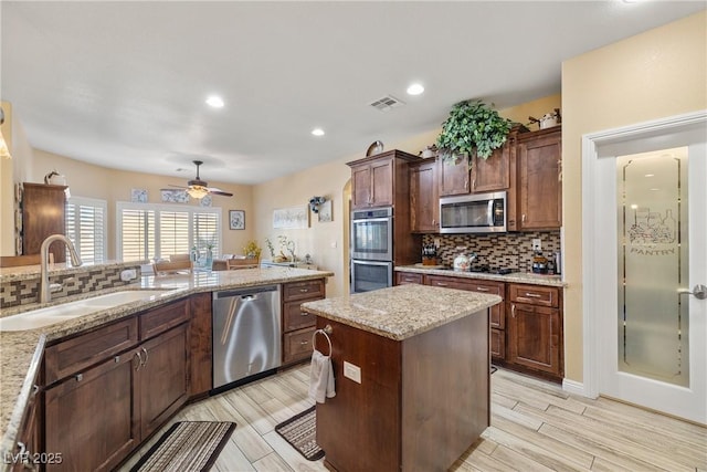 kitchen featuring sink, ceiling fan, light stone countertops, appliances with stainless steel finishes, and a kitchen island