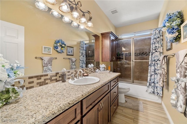 full bathroom featuring hardwood / wood-style floors, vanity, bath / shower combo with glass door, toilet, and tasteful backsplash