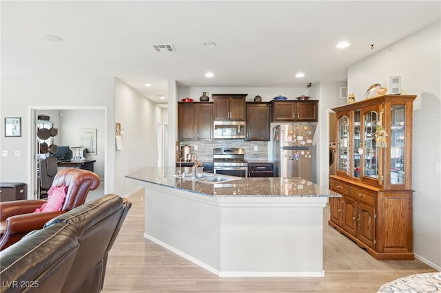 kitchen featuring sink, stainless steel appliances, light stone counters, decorative backsplash, and a center island with sink