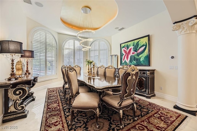 dining space featuring a raised ceiling, ornate columns, and a chandelier