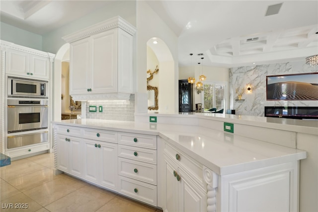 kitchen with decorative backsplash, appliances with stainless steel finishes, kitchen peninsula, decorative light fixtures, and white cabinetry