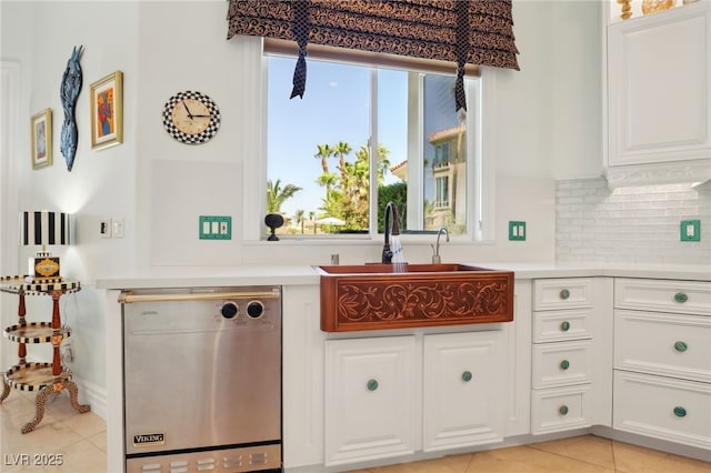 kitchen with white cabinetry, sink, stainless steel dishwasher, backsplash, and light tile patterned floors