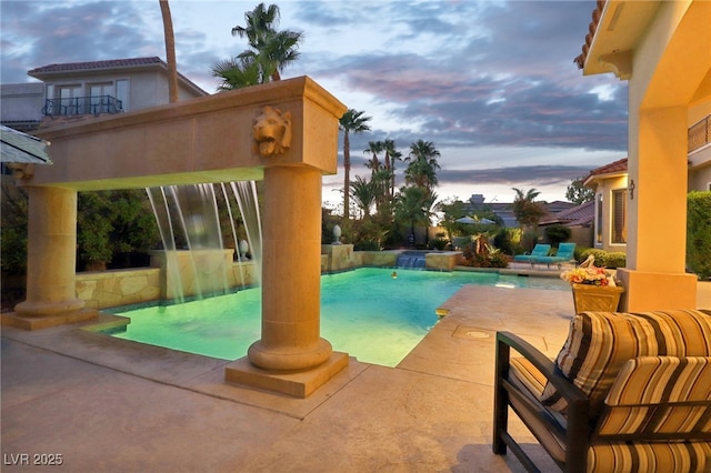 pool at dusk with a patio and pool water feature