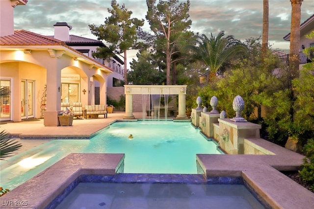 pool at dusk with a patio area, an in ground hot tub, and an outdoor hangout area