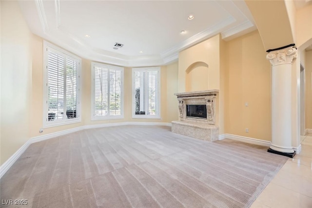 unfurnished living room featuring a fireplace, a tray ceiling, ornate columns, and light colored carpet