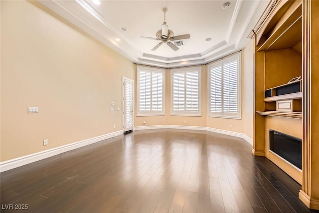 unfurnished living room featuring dark wood-type flooring, a raised ceiling, ceiling fan, and ornamental molding