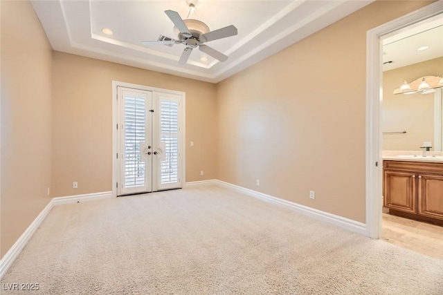 carpeted empty room featuring ceiling fan, a raised ceiling, sink, and french doors