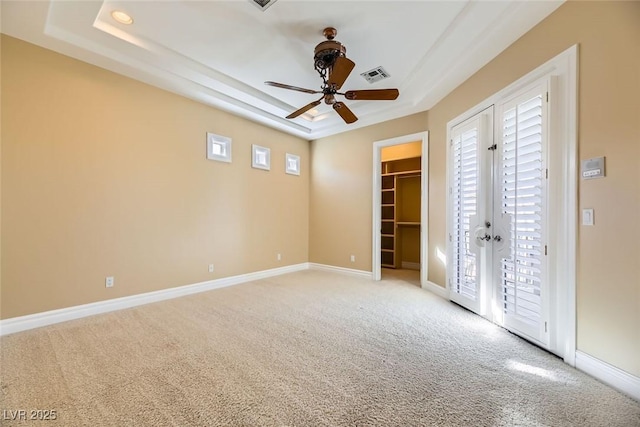 unfurnished bedroom featuring light carpet, a walk in closet, a raised ceiling, ceiling fan, and a closet