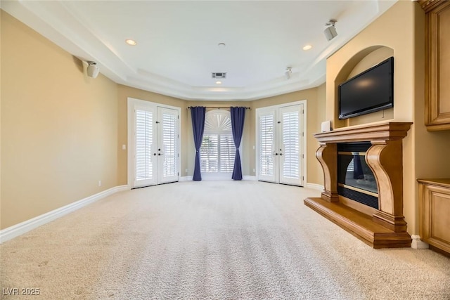 unfurnished living room with light carpet, french doors, a raised ceiling, and a wealth of natural light