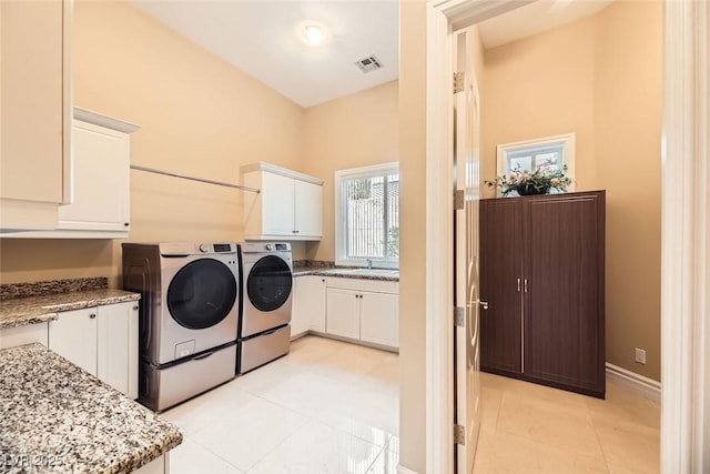 clothes washing area featuring washing machine and dryer, sink, light tile patterned floors, and cabinets