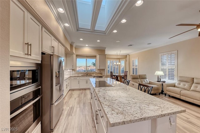 kitchen featuring light stone countertops, appliances with stainless steel finishes, crown molding, white cabinets, and a kitchen island