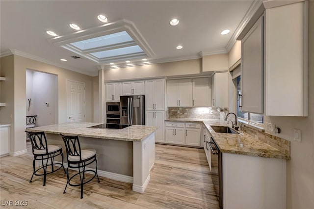 kitchen featuring a skylight, light stone countertops, sink, a kitchen island, and appliances with stainless steel finishes