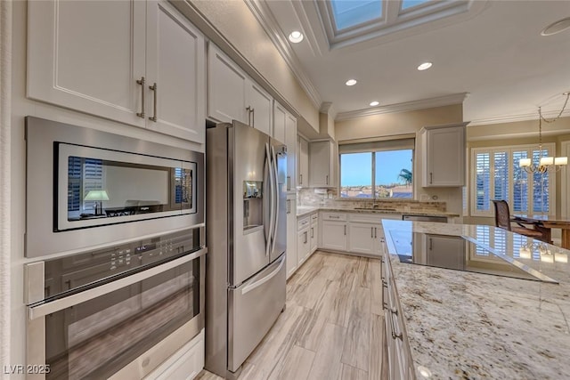 kitchen with light stone counters, a notable chandelier, crown molding, decorative light fixtures, and appliances with stainless steel finishes