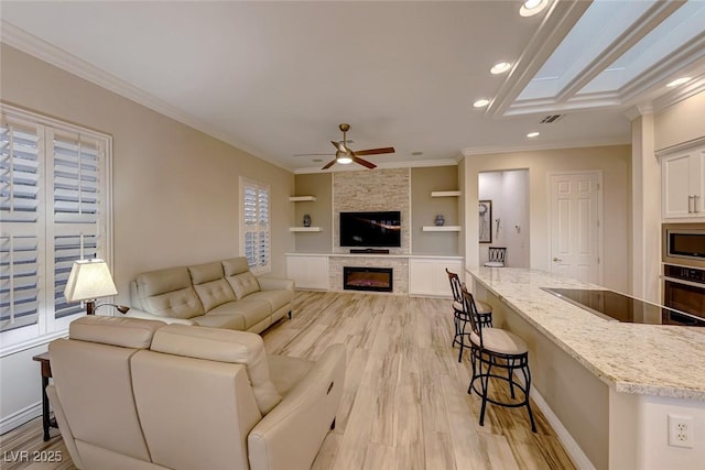 living room with crown molding, light hardwood / wood-style flooring, ceiling fan, built in features, and a fireplace