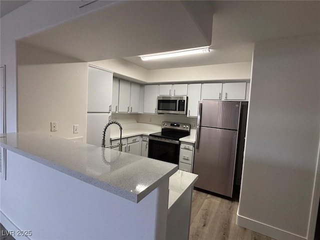 kitchen featuring white cabinetry, sink, light hardwood / wood-style flooring, kitchen peninsula, and appliances with stainless steel finishes