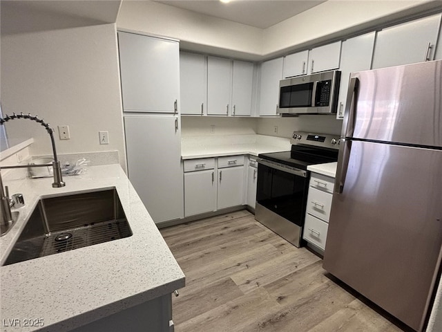 kitchen with light stone counters, stainless steel appliances, sink, light hardwood / wood-style flooring, and white cabinetry