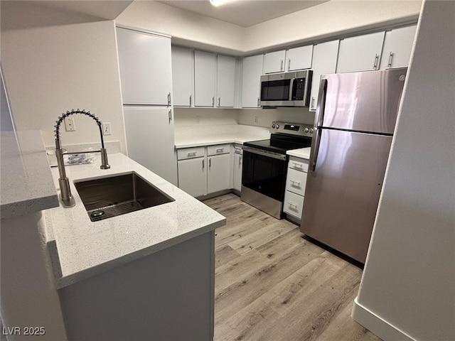 kitchen with white cabinets, appliances with stainless steel finishes, light wood-type flooring, and sink