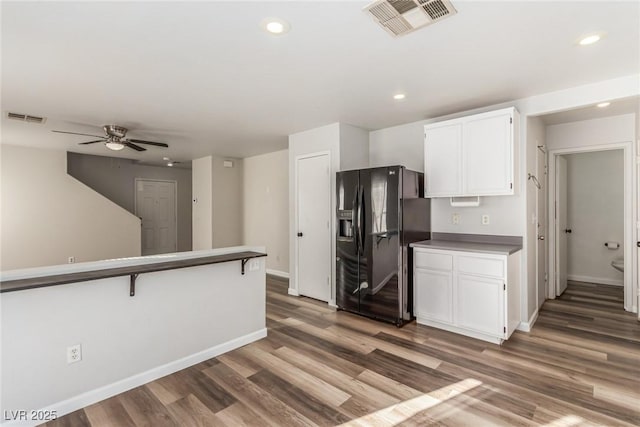 kitchen featuring a breakfast bar, black fridge with ice dispenser, ceiling fan, dark hardwood / wood-style floors, and white cabinetry