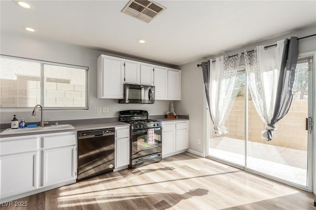 kitchen with black appliances, light hardwood / wood-style floors, white cabinets, and sink