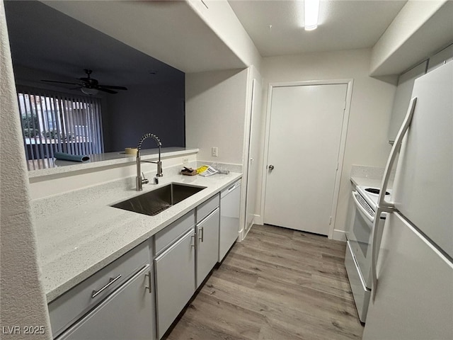 kitchen featuring white appliances, white cabinets, sink, light wood-type flooring, and light stone counters