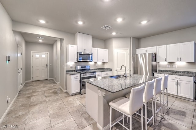 kitchen with appliances with stainless steel finishes, white cabinetry, an island with sink, sink, and a kitchen bar