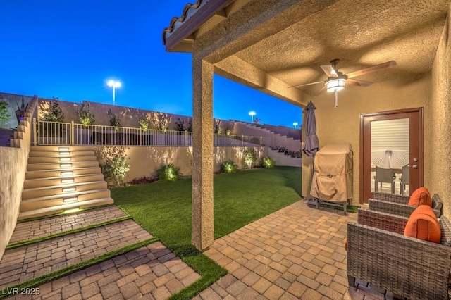 patio terrace at dusk featuring ceiling fan and a lawn