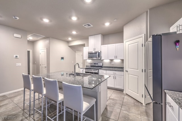 kitchen featuring a breakfast bar, sink, appliances with stainless steel finishes, an island with sink, and dark stone counters