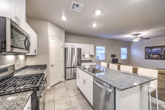 kitchen featuring sink, appliances with stainless steel finishes, white cabinetry, an island with sink, and a kitchen bar