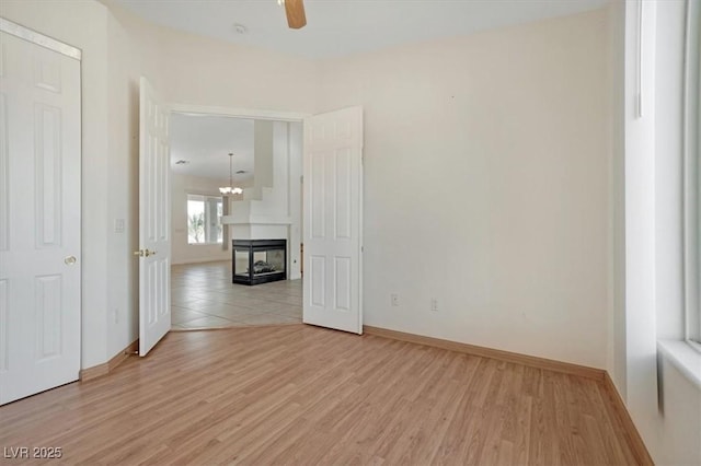 unfurnished room featuring a multi sided fireplace, light wood-type flooring, and ceiling fan with notable chandelier