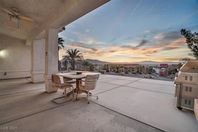 patio terrace at dusk featuring a mountain view and ceiling fan