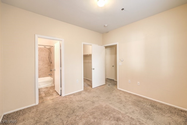 unfurnished bedroom featuring ensuite bathroom, a spacious closet, light carpet, and a closet