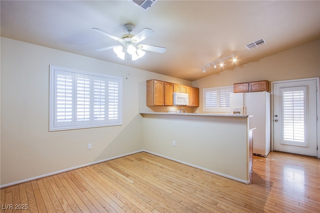 kitchen with light hardwood / wood-style floors, lofted ceiling, white appliances, and kitchen peninsula