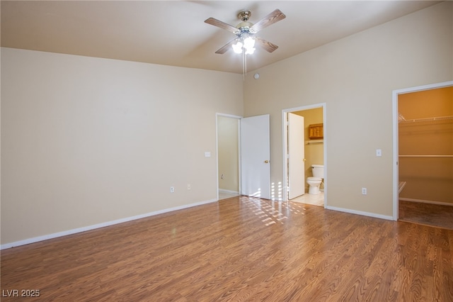 unfurnished bedroom with ensuite bath, ceiling fan, wood-type flooring, a spacious closet, and a closet