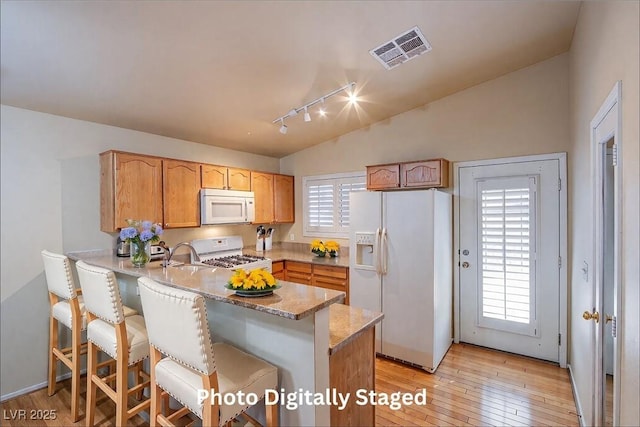 kitchen featuring lofted ceiling, a breakfast bar area, light hardwood / wood-style flooring, kitchen peninsula, and white appliances