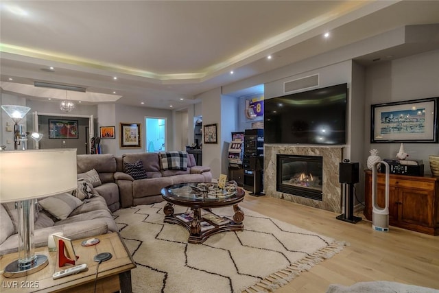 living room featuring a high end fireplace, light wood-type flooring, and a tray ceiling