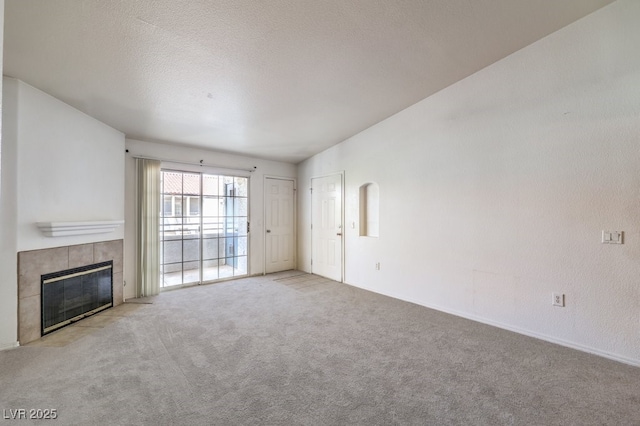 unfurnished living room featuring a tiled fireplace, light colored carpet, and a textured ceiling