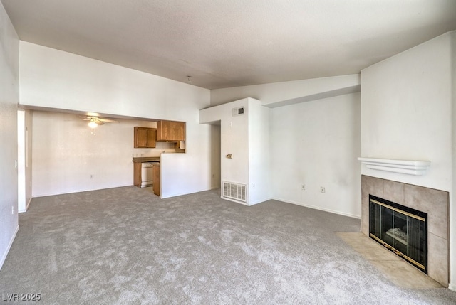 unfurnished living room featuring a tiled fireplace, ceiling fan, light colored carpet, and vaulted ceiling