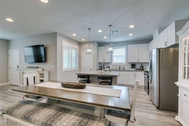 kitchen with pendant lighting, black electric range oven, white cabinets, stainless steel fridge, and an island with sink