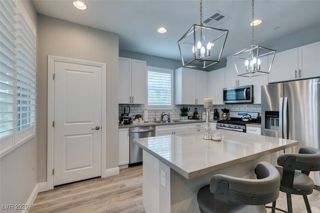 kitchen with white cabinetry, a center island, stainless steel appliances, pendant lighting, and a breakfast bar area