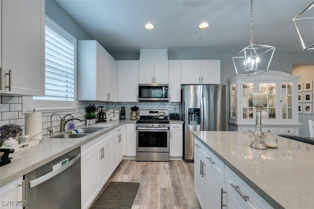 kitchen with white cabinetry, sink, stainless steel appliances, and a notable chandelier