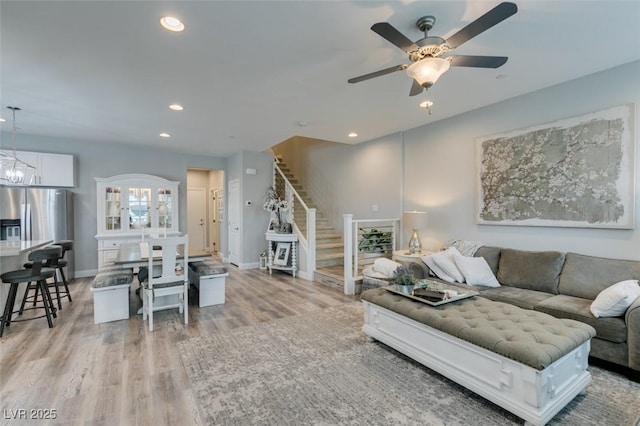 living room featuring ceiling fan with notable chandelier and light wood-type flooring