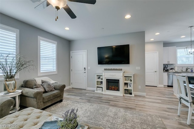 living room featuring light wood-type flooring, ceiling fan with notable chandelier, and sink