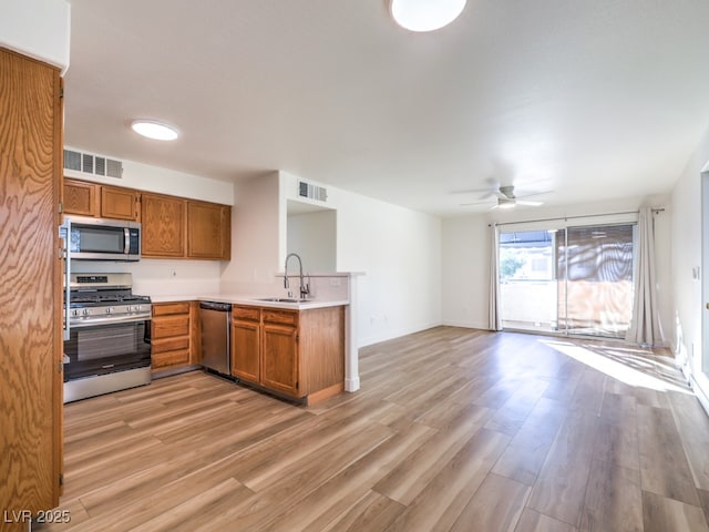 kitchen with sink, ceiling fan, appliances with stainless steel finishes, light hardwood / wood-style floors, and kitchen peninsula