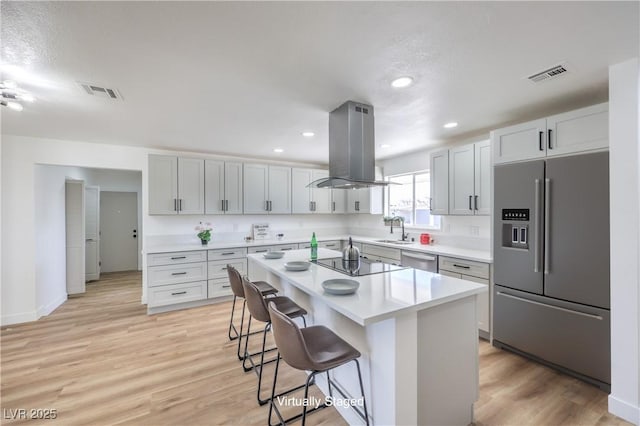 kitchen featuring sink, a kitchen island, island range hood, a kitchen bar, and stainless steel appliances