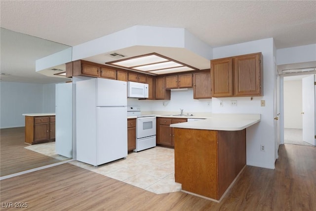 kitchen with kitchen peninsula, white appliances, light wood-type flooring, a textured ceiling, and sink