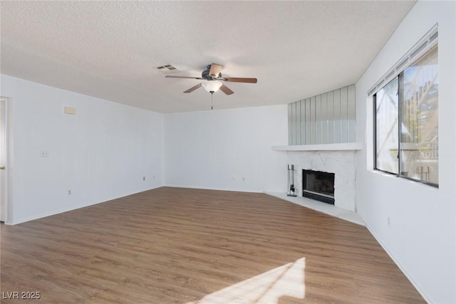 unfurnished living room with a textured ceiling, a premium fireplace, wood-type flooring, and ceiling fan