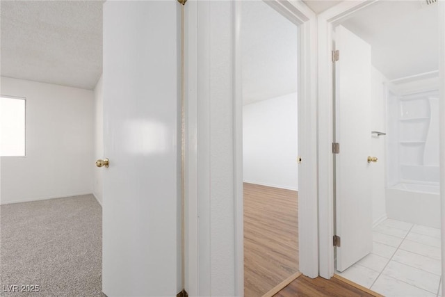 hall with a textured ceiling and light colored carpet