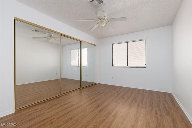 unfurnished bedroom featuring a textured ceiling, a closet, wood-type flooring, and ceiling fan